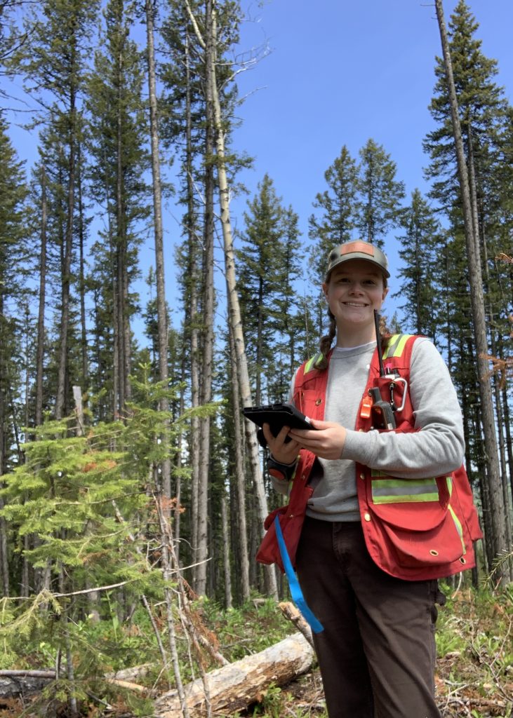 UBC Forestry Co-op student, Ainsley Hannah, wearing safety gear while holding a booklet and standing in the forest. 