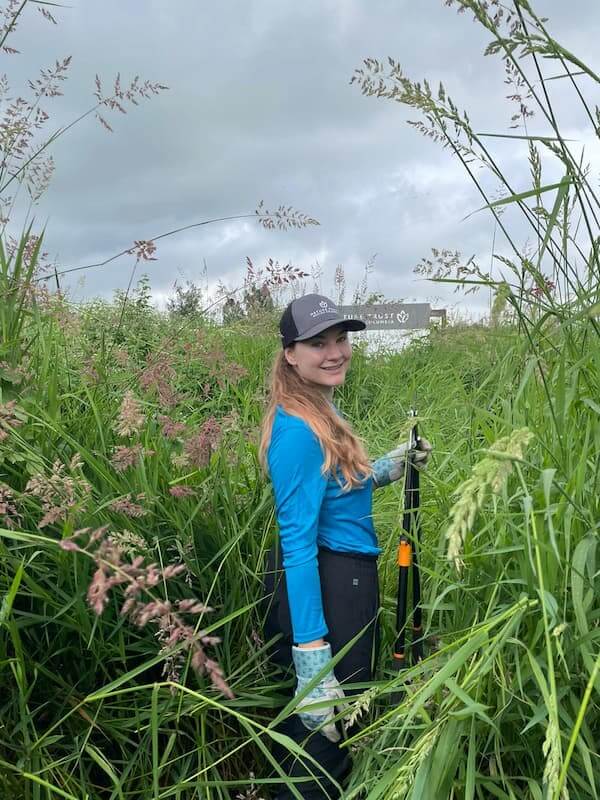 Mikayla Faucett, UBC Forestry Co-op student, standing in a field of plants while smiling.