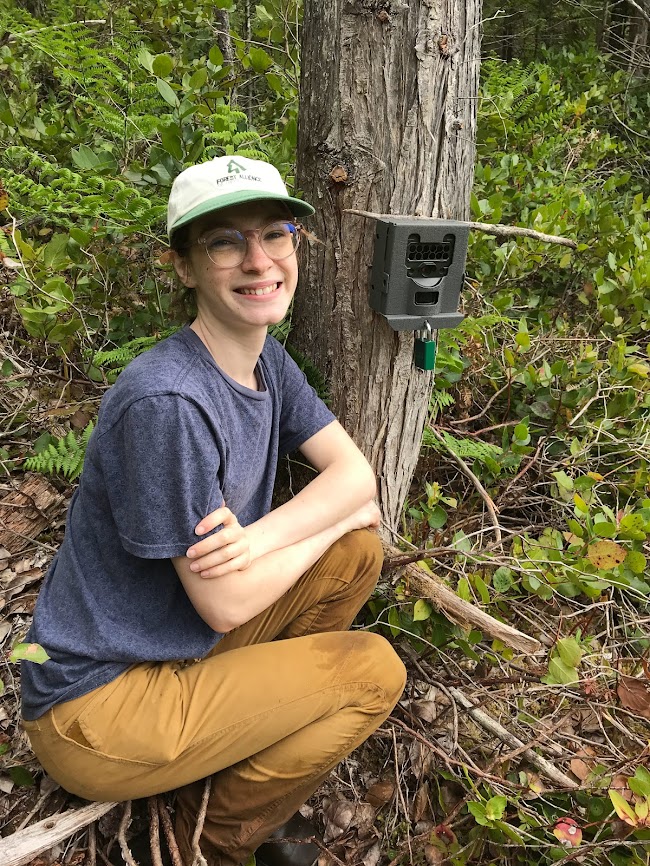 Tristen kneeling near a tree camera and smiling.