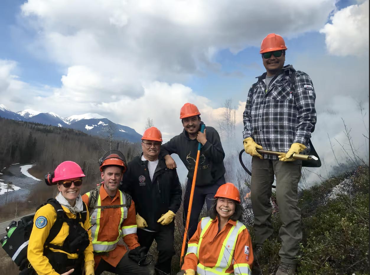Researchers pose in high-vis vests and hard hats in front of mountains.
