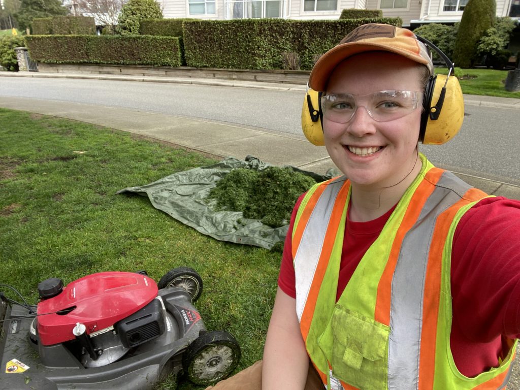 Anya standing in front of a lawn mower and smiling.