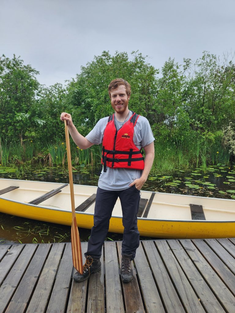 Jonathan holding a paddle and smiling in front of a boat.