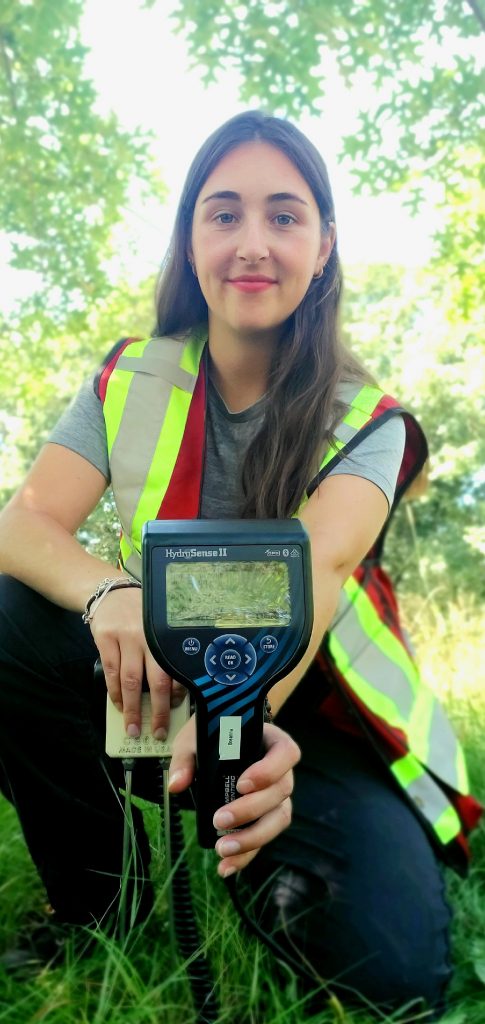 Breanna showing the camera a tree inspection device and smiling.