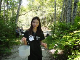 UBC Forestry Co-op Student, Jennie is looking at the camera smiling while holding a bucket in the forest.