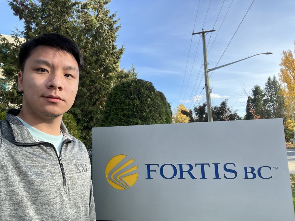 UBC Forestry student, Victor taking a selfie with the sign of the FortisBC outdoors.